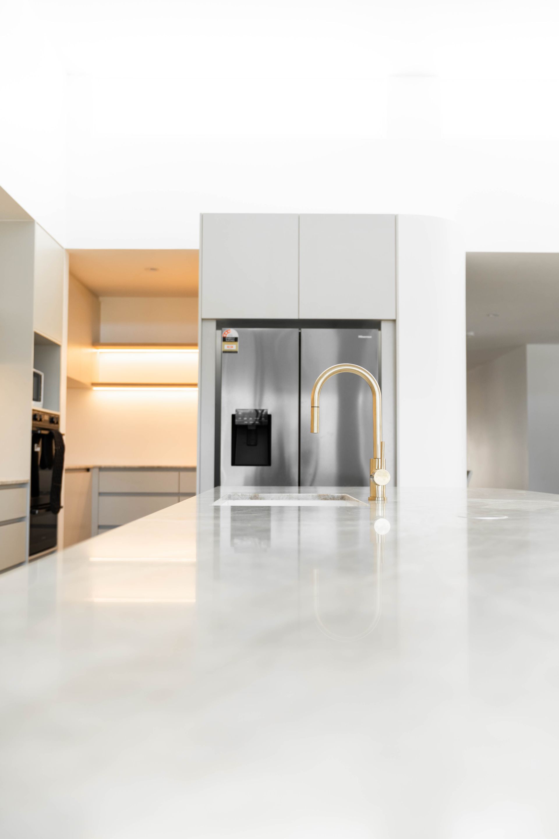 Modern kitchen featuring a long, white marble island, a stainless steel refrigerator, and a gold-colored faucet.