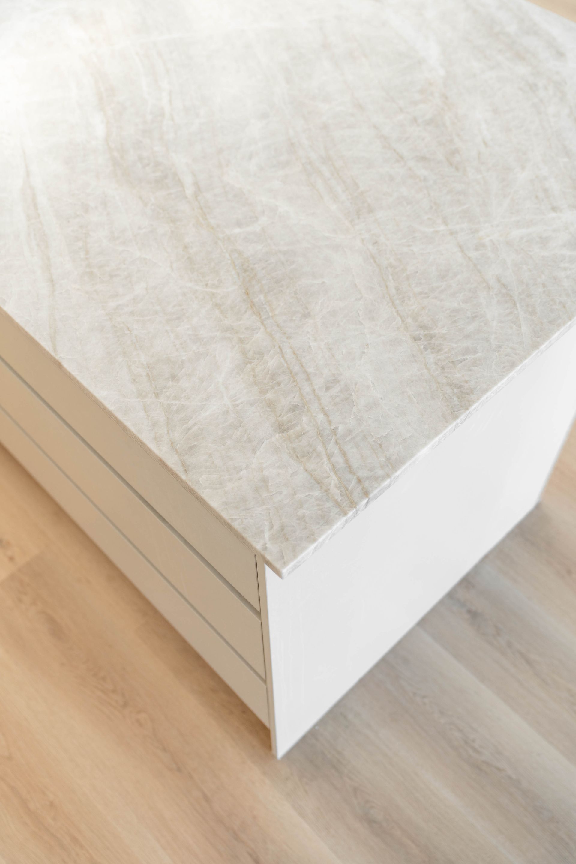 A white cabinet with a light, marbled stone countertop sits on a wooden floor, viewed from a high angle.