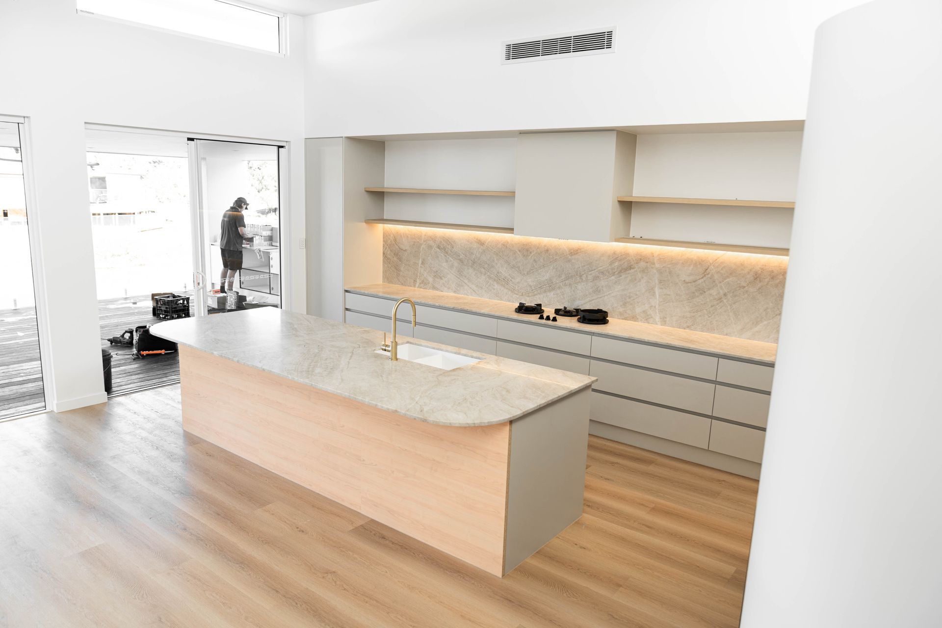 A modern kitchen with a light wood island, grey lower cabinets, floating shelves, and herringbone tile backsplash.