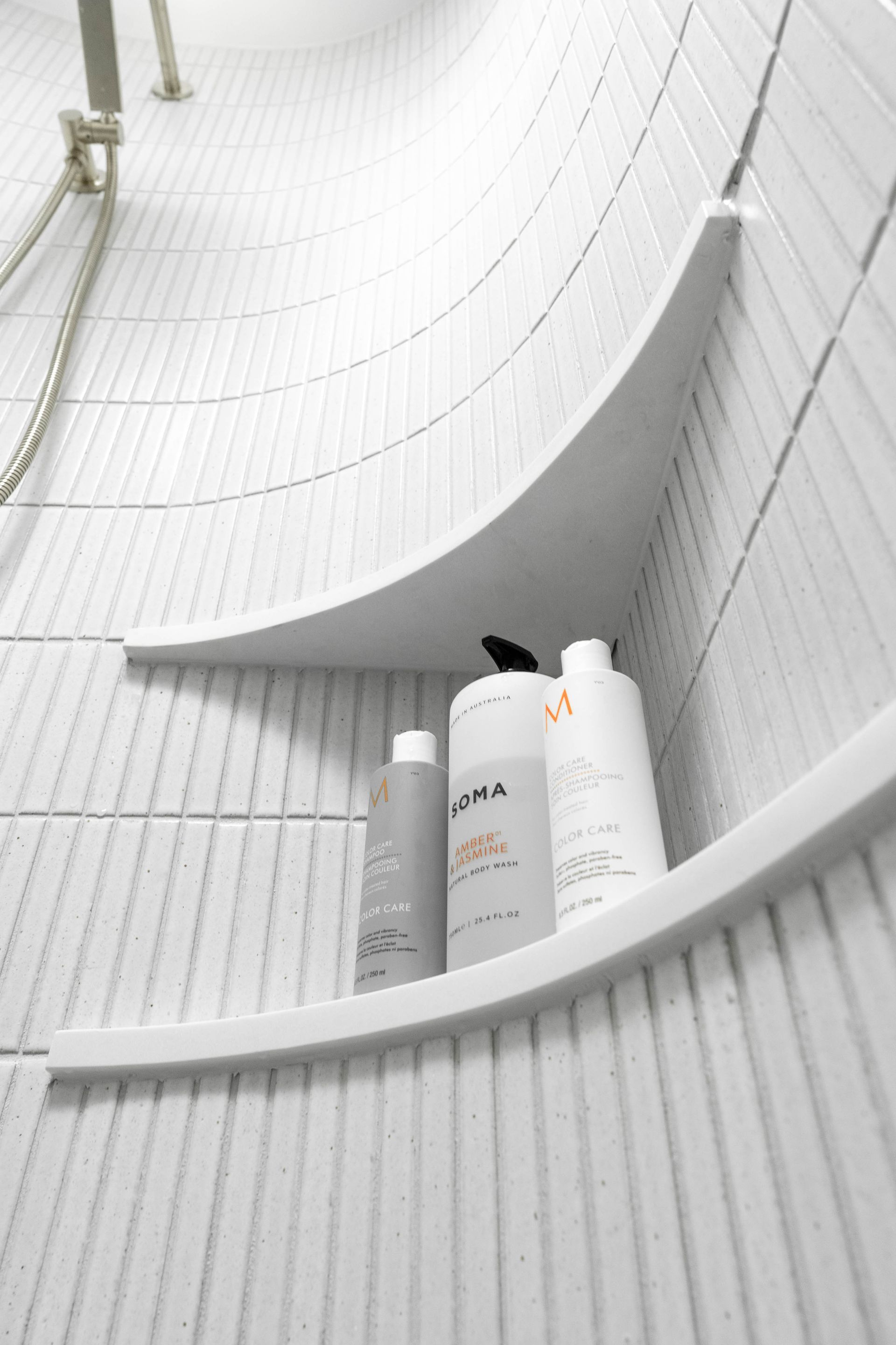 White curved shower wall with a built-in shelf holding three bottles of toiletries.