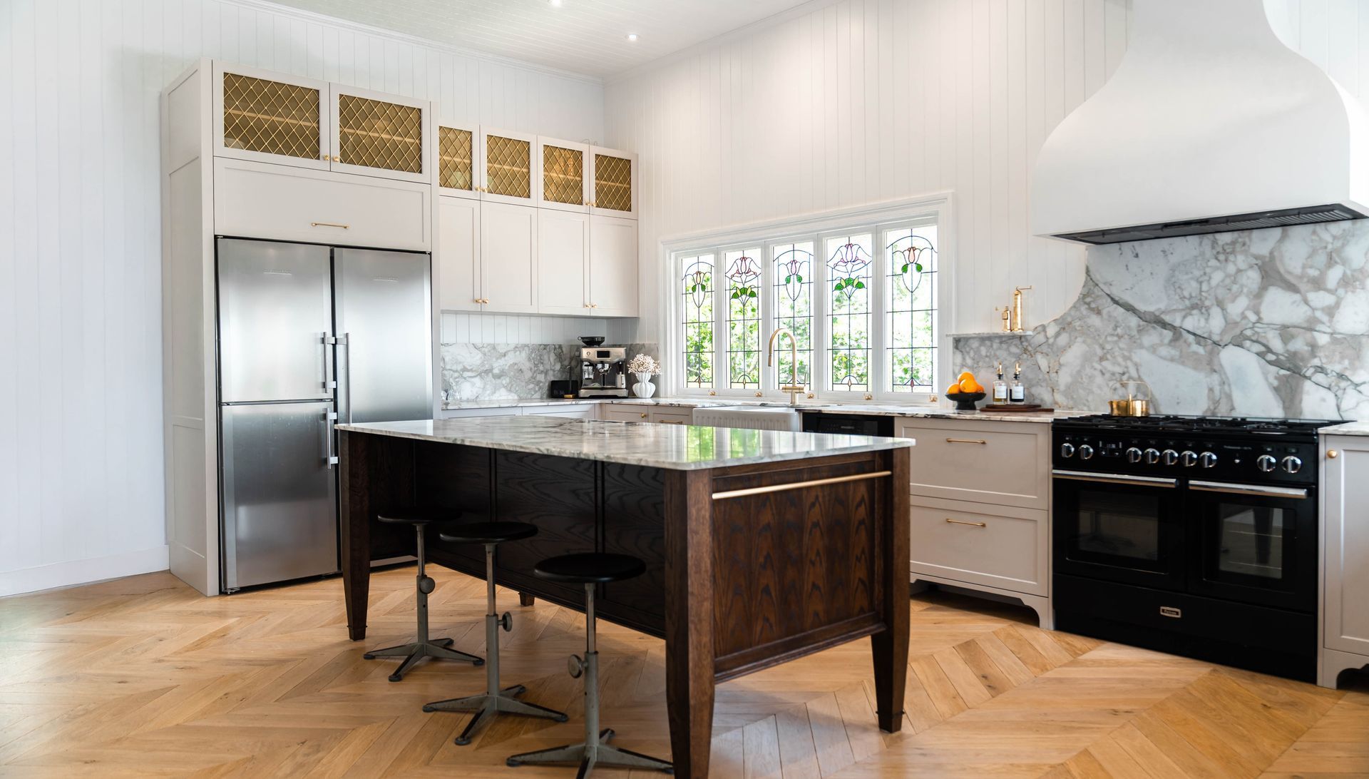 A modern kitchen features white cabinets, a dark wood island with three bar stools, a stainless fridge, and a black stove.