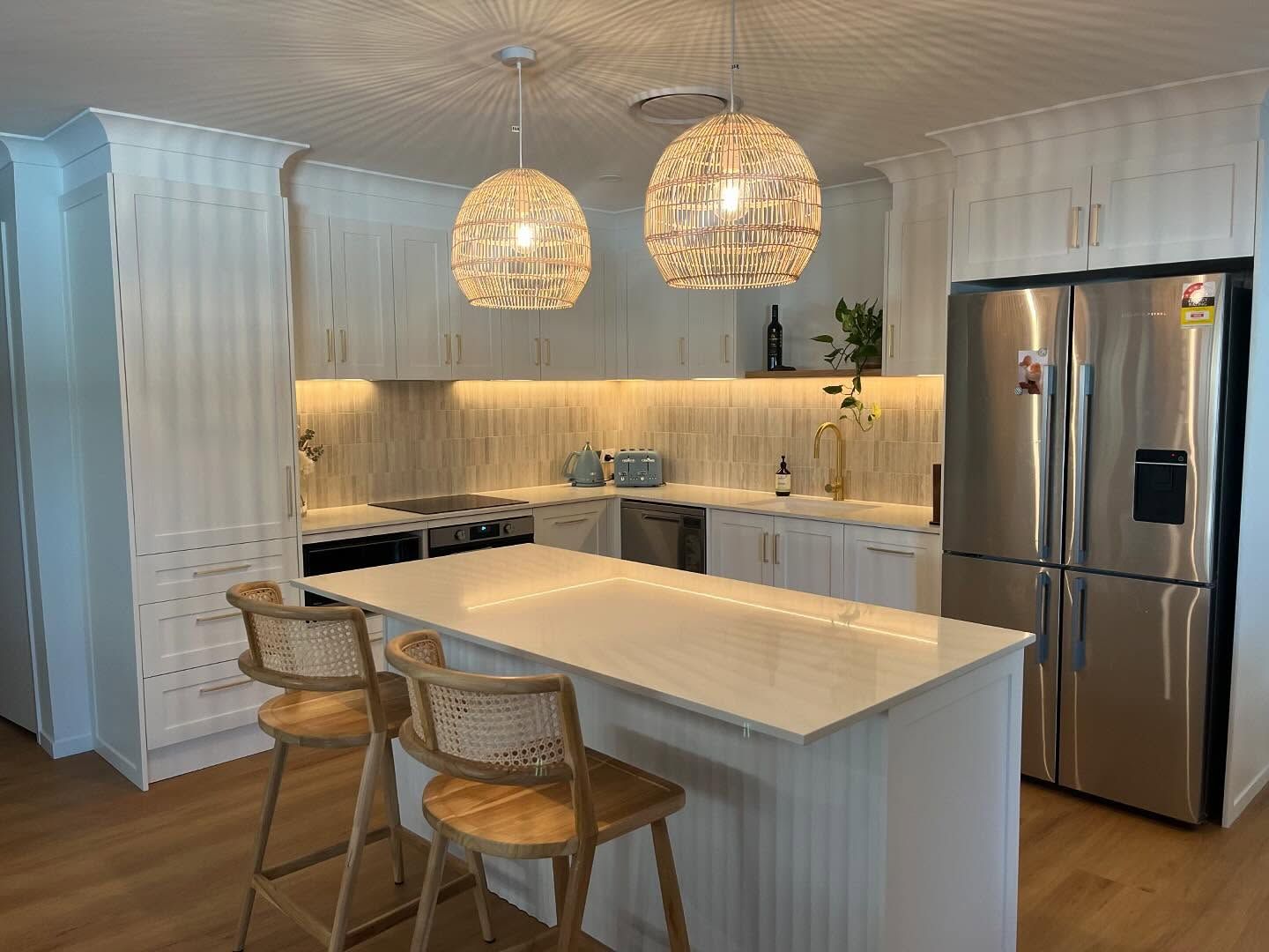 Coastal-style kitchen with stone benchtops on the Gold Coast, featuring a fluted island, rattan pendant lights, matching stone splashback and brass hardware