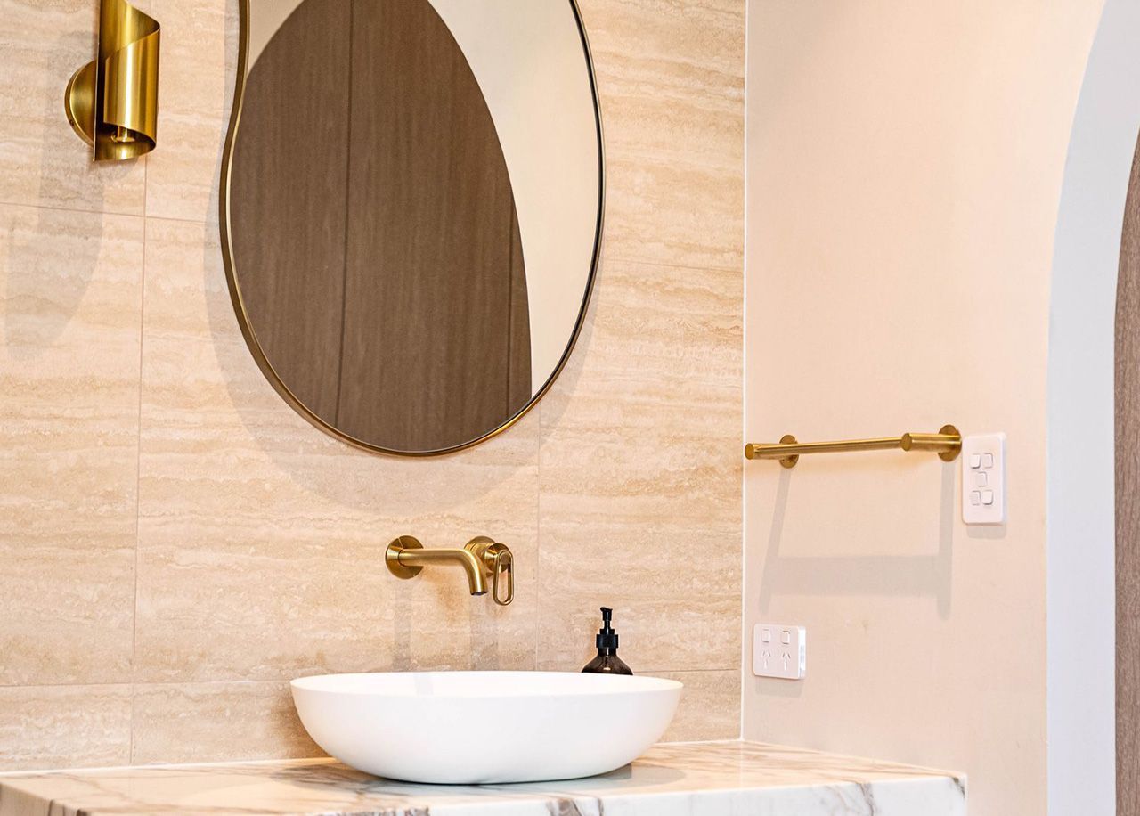 Luxury bathroom vanity with stone benchtops on the Gold Coast featuring a vessel basin, brushed brass wall-mounted tapware and travertine wall tiles
