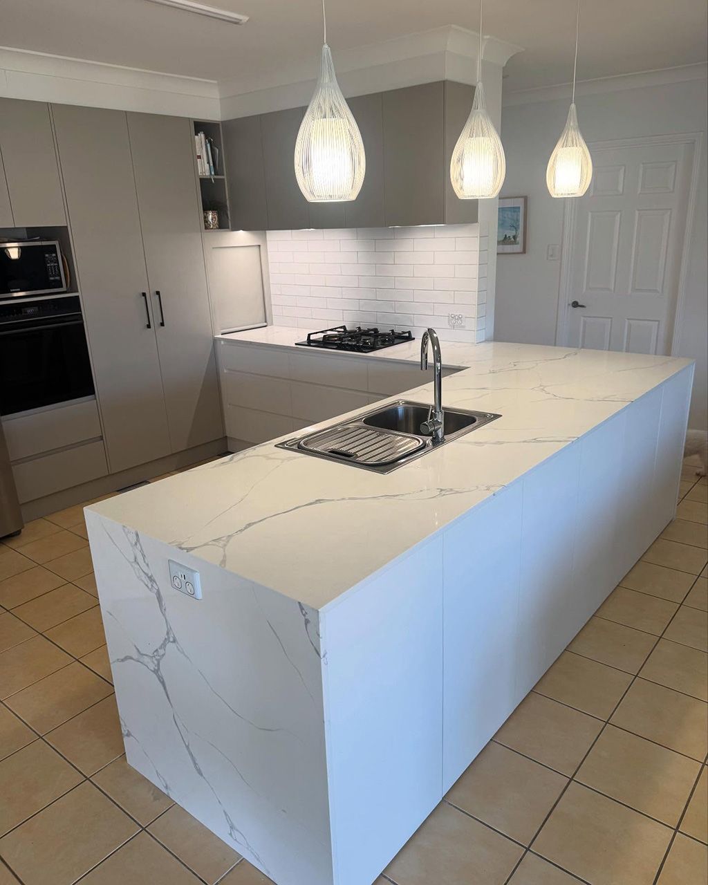 Kitchen island featuring custom stone benchtops on the Gold Coast with a white marble finish, integrated sink and white subway tile splashback