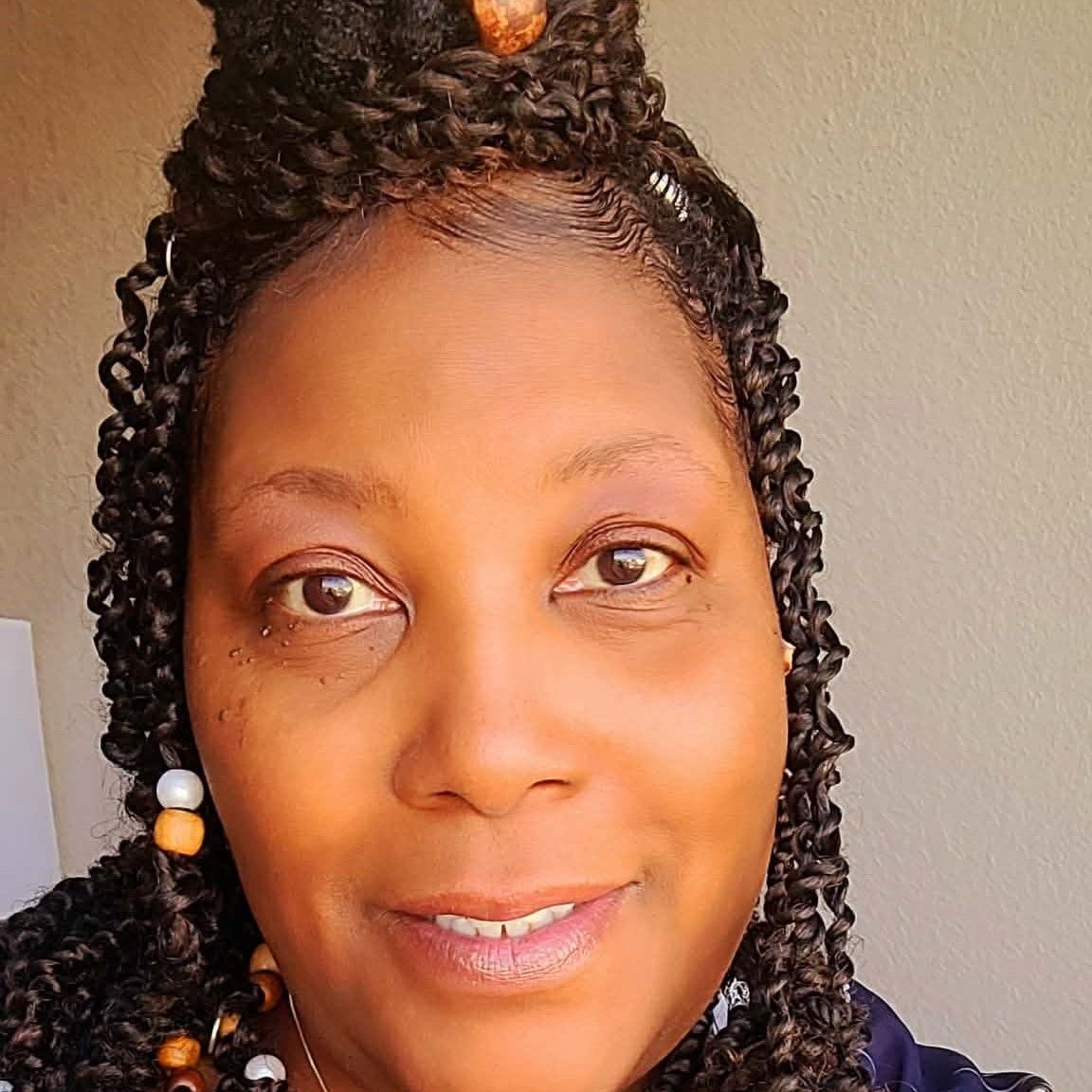 Close-up portrait of a smiling woman with braided hair and colorful beads against a plain background