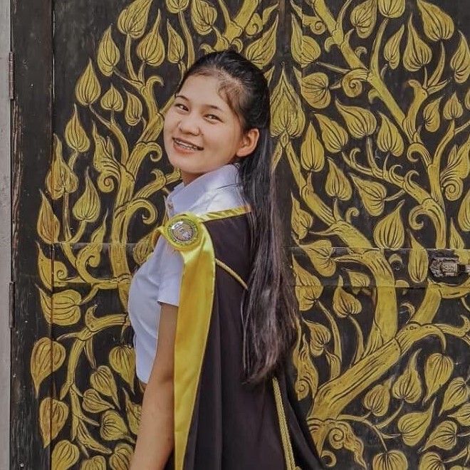 Woman in graduation attire smiles, stands before ornate gold and black door.