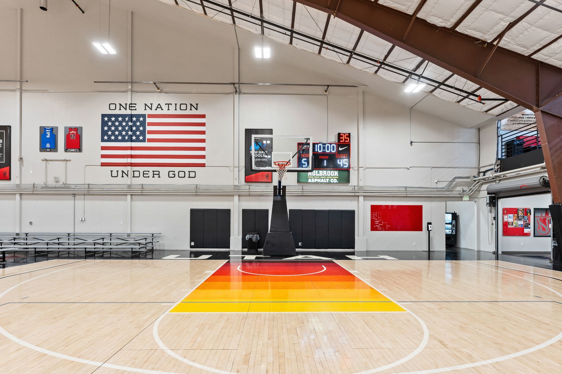 A large indoor basketball court with an american flag on the wall.