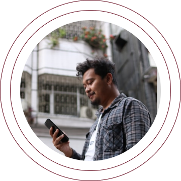 Man holding a smartphone outdoors in front of a modern building, wearing a plaid shirt