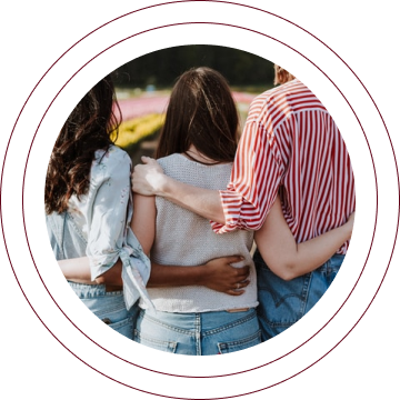 Three friends walking arm-in-arm outdoors, seen from behind in casual jeans and shirts.