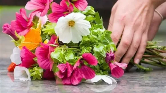 Hand arranging a bouquet of pink, white, and orange flowers on a table