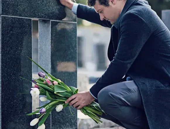 Man placing purple tulips at a stone grave marker in a cemetery