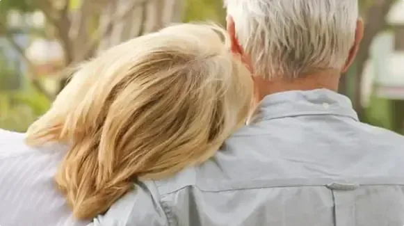 Two people seen from behind, one resting their head on the other’s shoulder outdoors