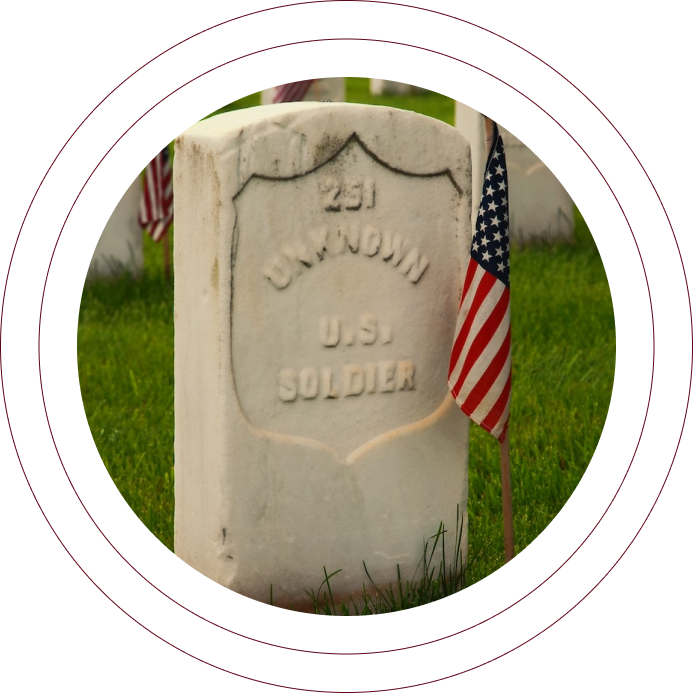 Liberty monument gravestone with a small American flag in a grassy cemetery