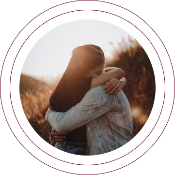 Two people hugging outdoors at sunset, framed by a circular border