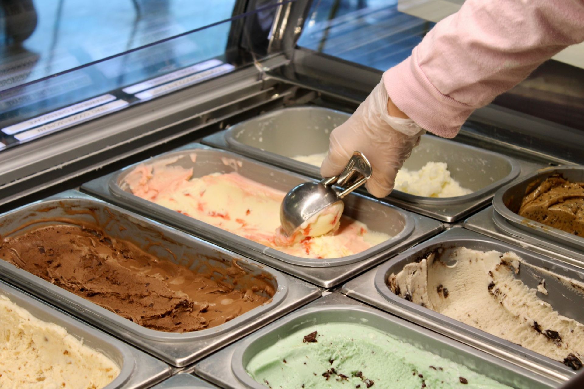 Hand scooping gelato from a display case with assorted gelato flavors