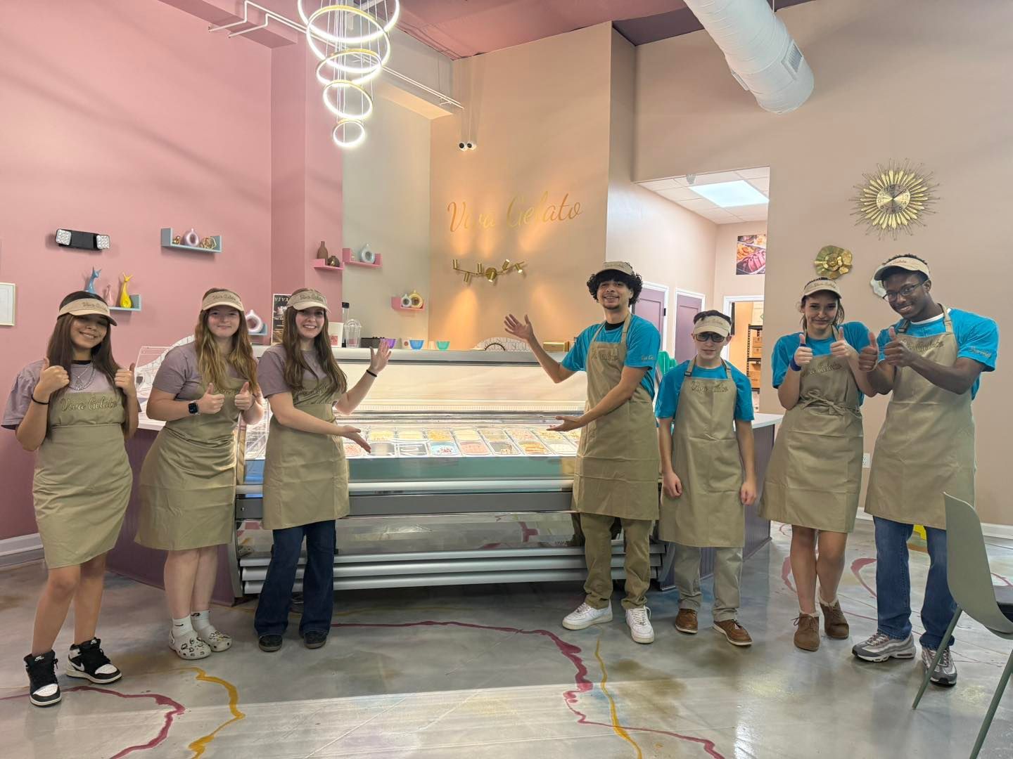 Group of people in aprons and hats standing around a lit display case in viva gelato smiling and posing