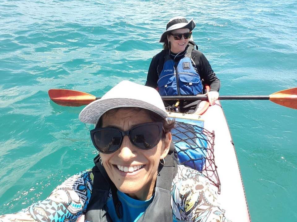 Two people kakaking on clear turquoise water, smiling and wearing hats and sunglasses in the Galapagos Islands.