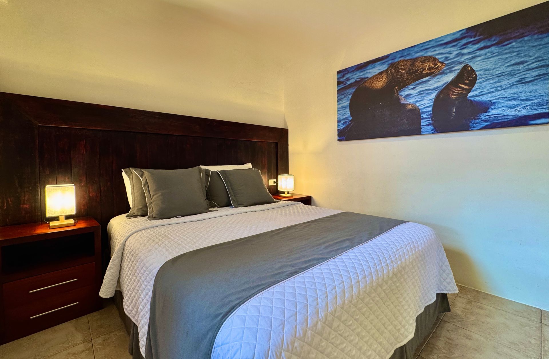 Neatly made bed in a warm-toned hotel room with bedside lamps and wall art