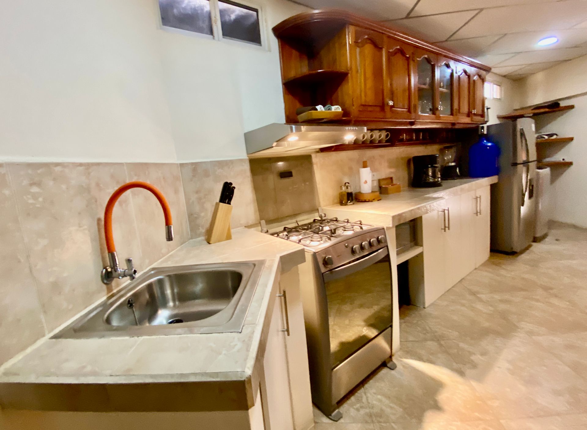 A Galapagos hotel with wooden cabinets, a stainless steel stove, sink, and refrigerator. The walls are light-colored.