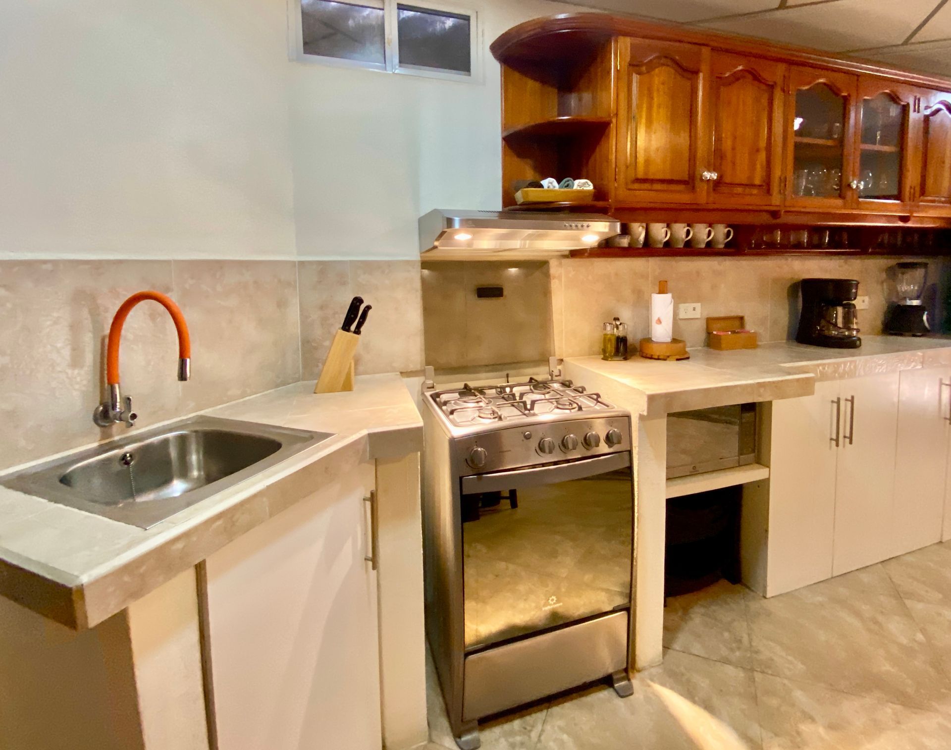 Hotel suite kitchen with stainless sink, gas stove, beige countertops, and wooden cabinets