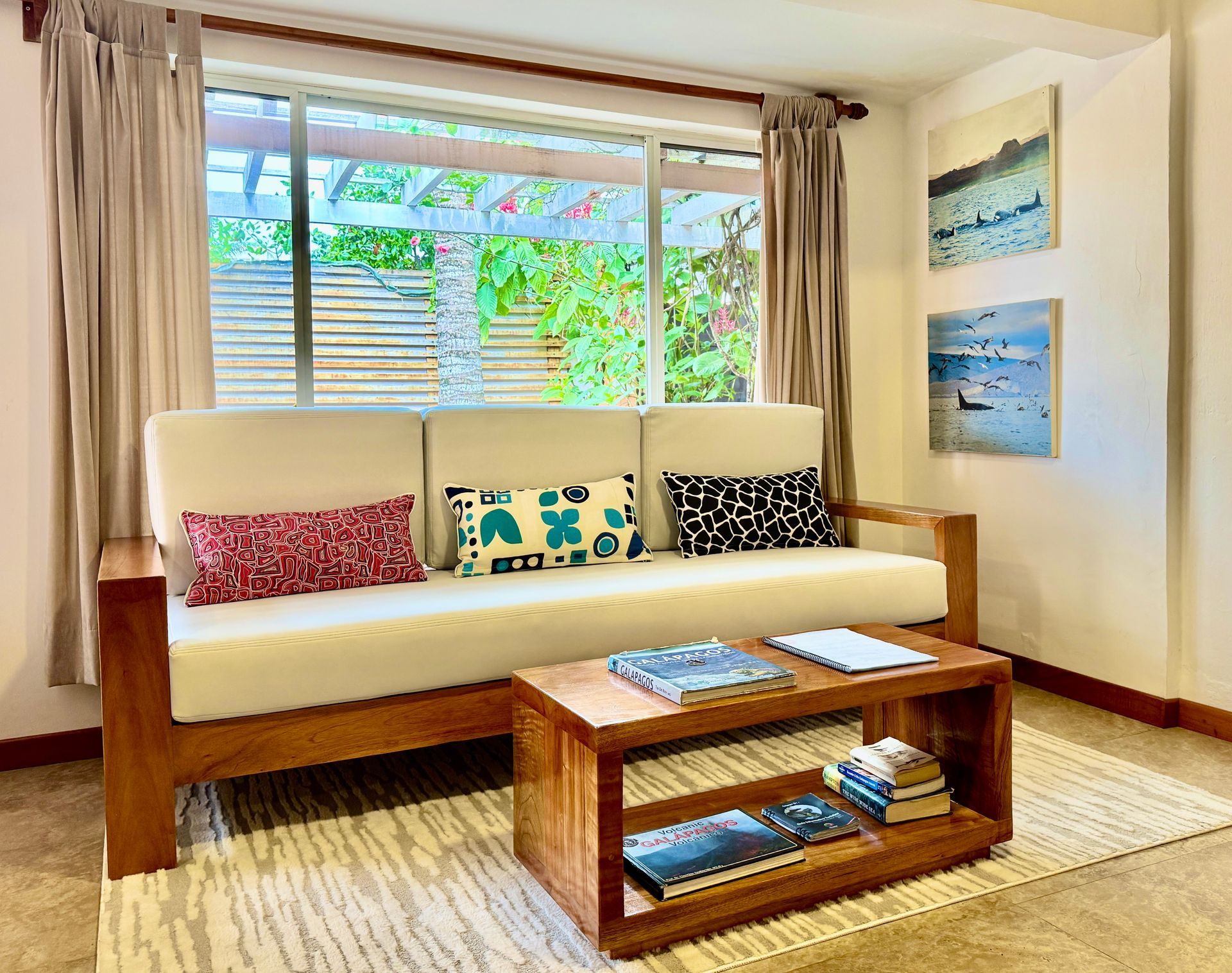 Bright living room with white sofa, wooden coffee table, and large window with beige curtains.