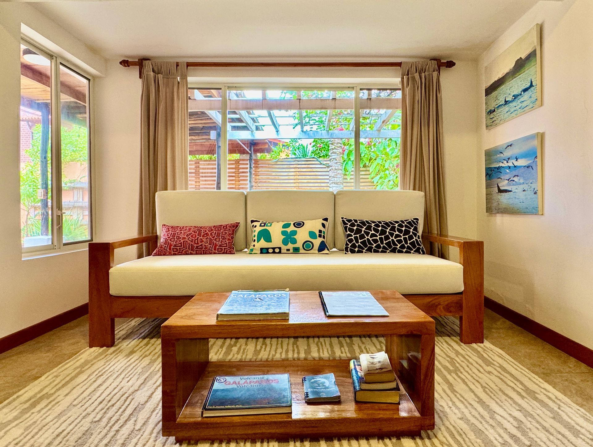Galapagos hotel Living room with cream-colored sofa, wooden coffee table, and artwork on the wall. A large window looks out onto greenery.