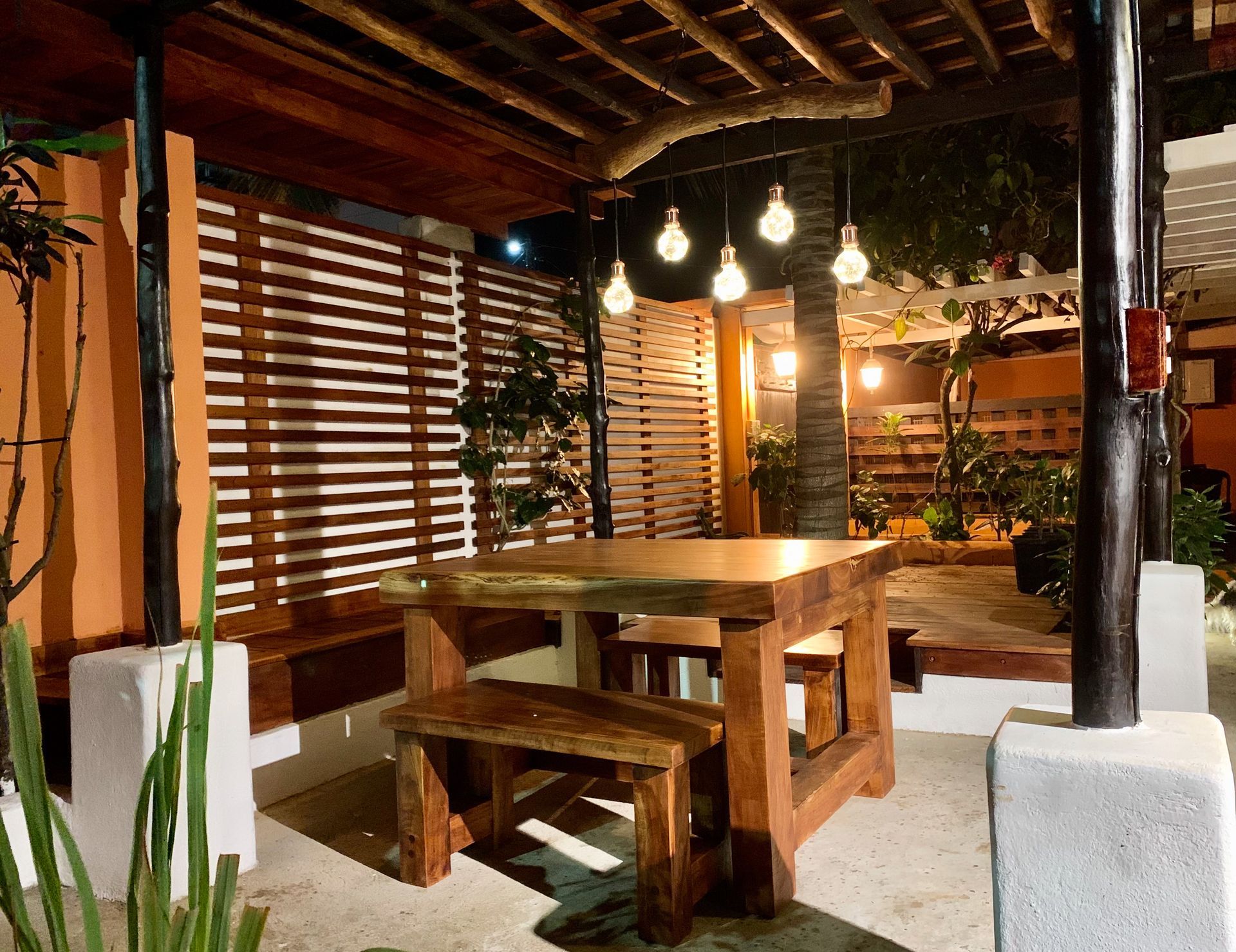 A Galapagos hotel outdoor dining area with wooden table, benches, hanging lights, and plants at night