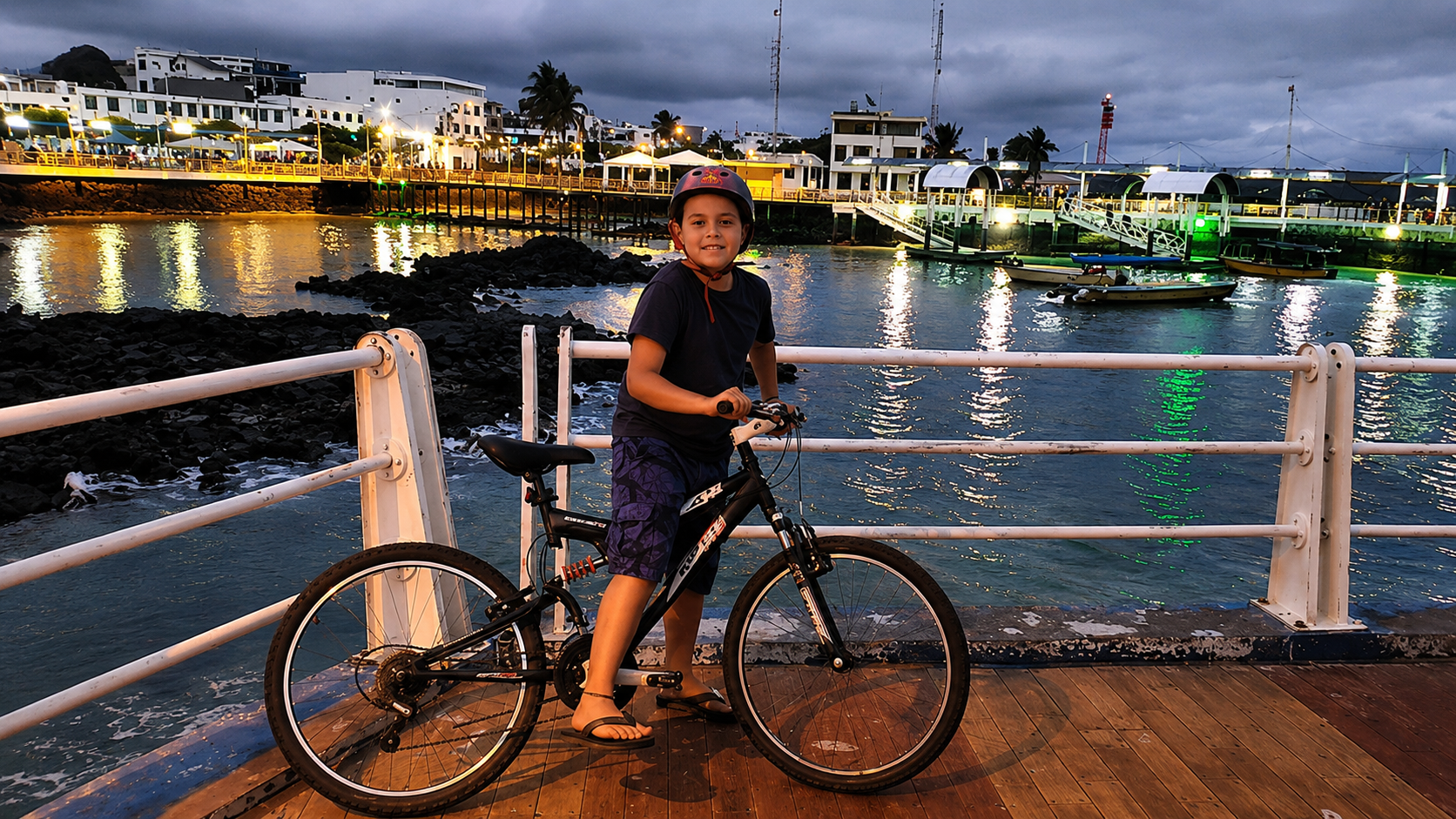 A child on a bicycle by a waterfront at dusk, with harbor lights reflecting on the water in the Galapagos.