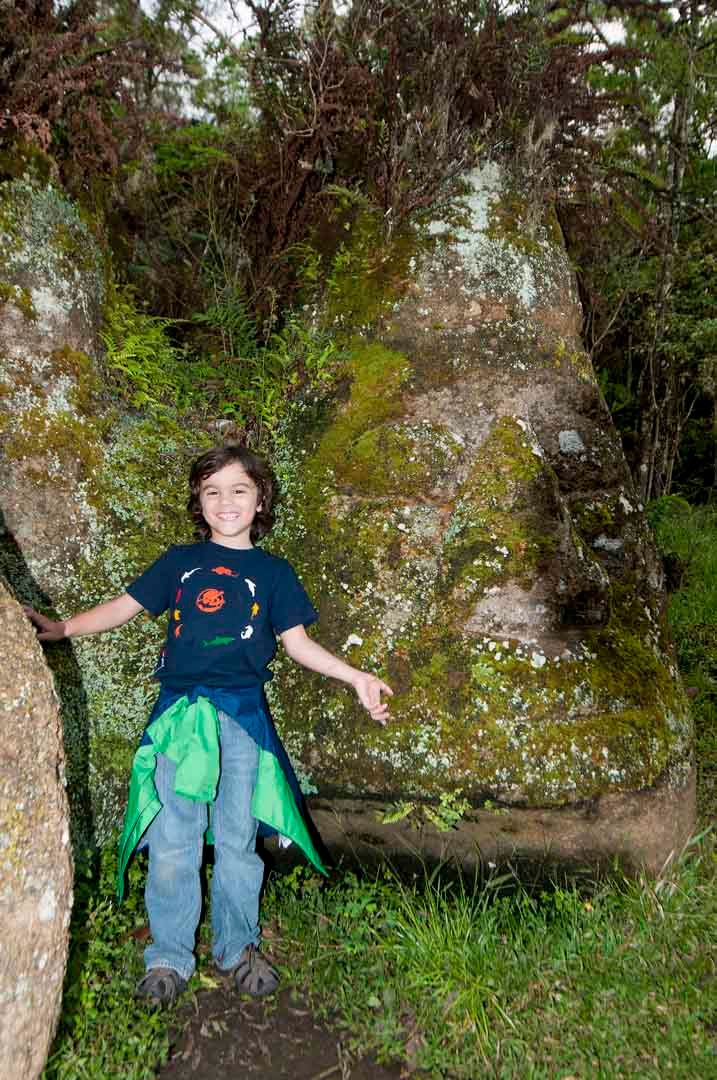 A young boy is standing next to a large rock in the woods in Galapagos.