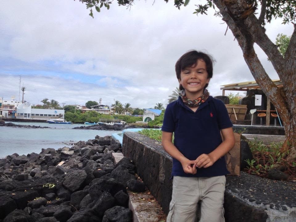 Smiling child standing on rocks by the waterfront under cloudy sky