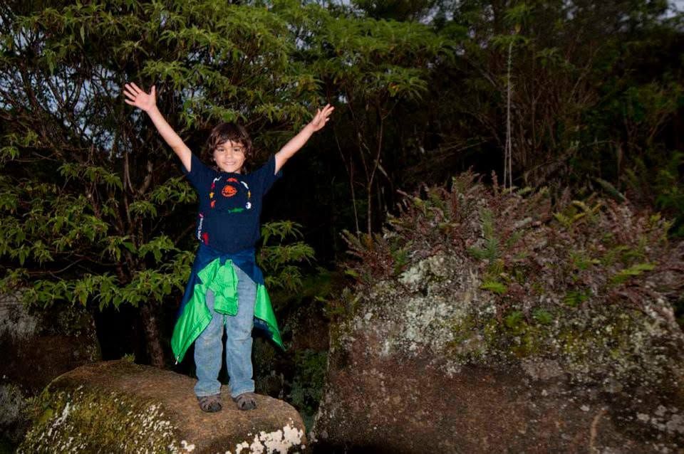 Person standing on a rock with arms raised, wearing a dark shirt and green jacket in a wooded area at night