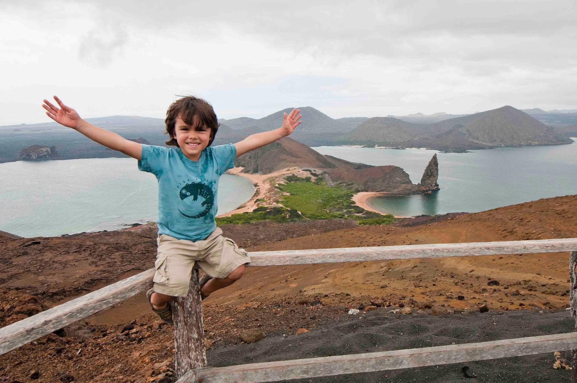 Child jumping with arms outstretched on a scenic overlook above a rocky bay and mountains