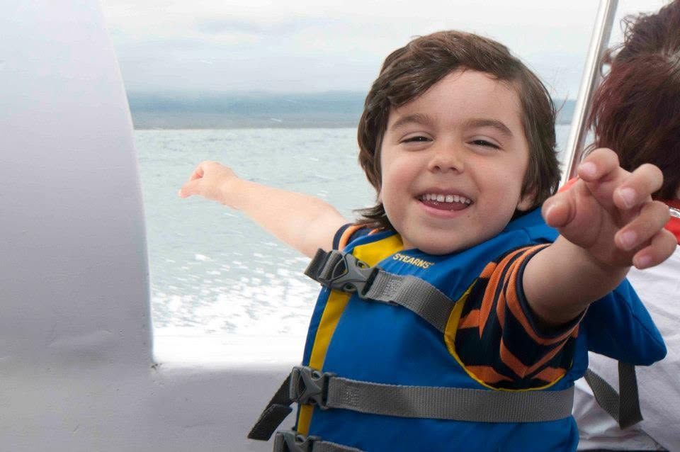 Smiling child in a blue life vest reaching out on a boat with ocean in the background