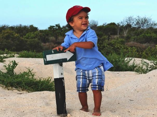 Child in a red cap standing by a path direction in a sandy beach, smiling and looking left.