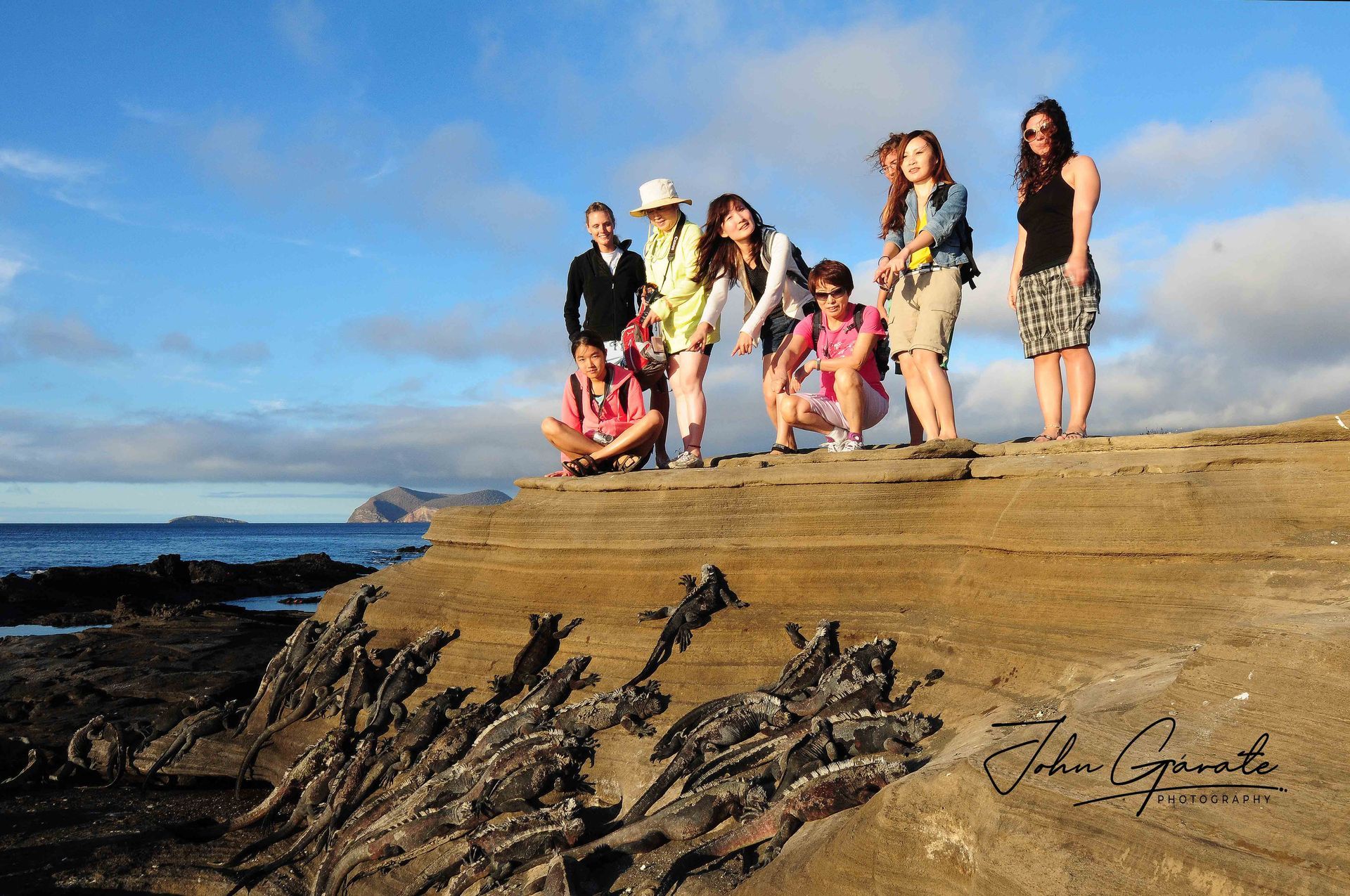 Group standing on a rocky cliff by the ocean under a blue sky.