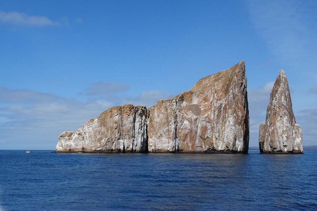 Two sea stacks rising from a calm blue ocean under a clear sky in the Galapagos Islands.