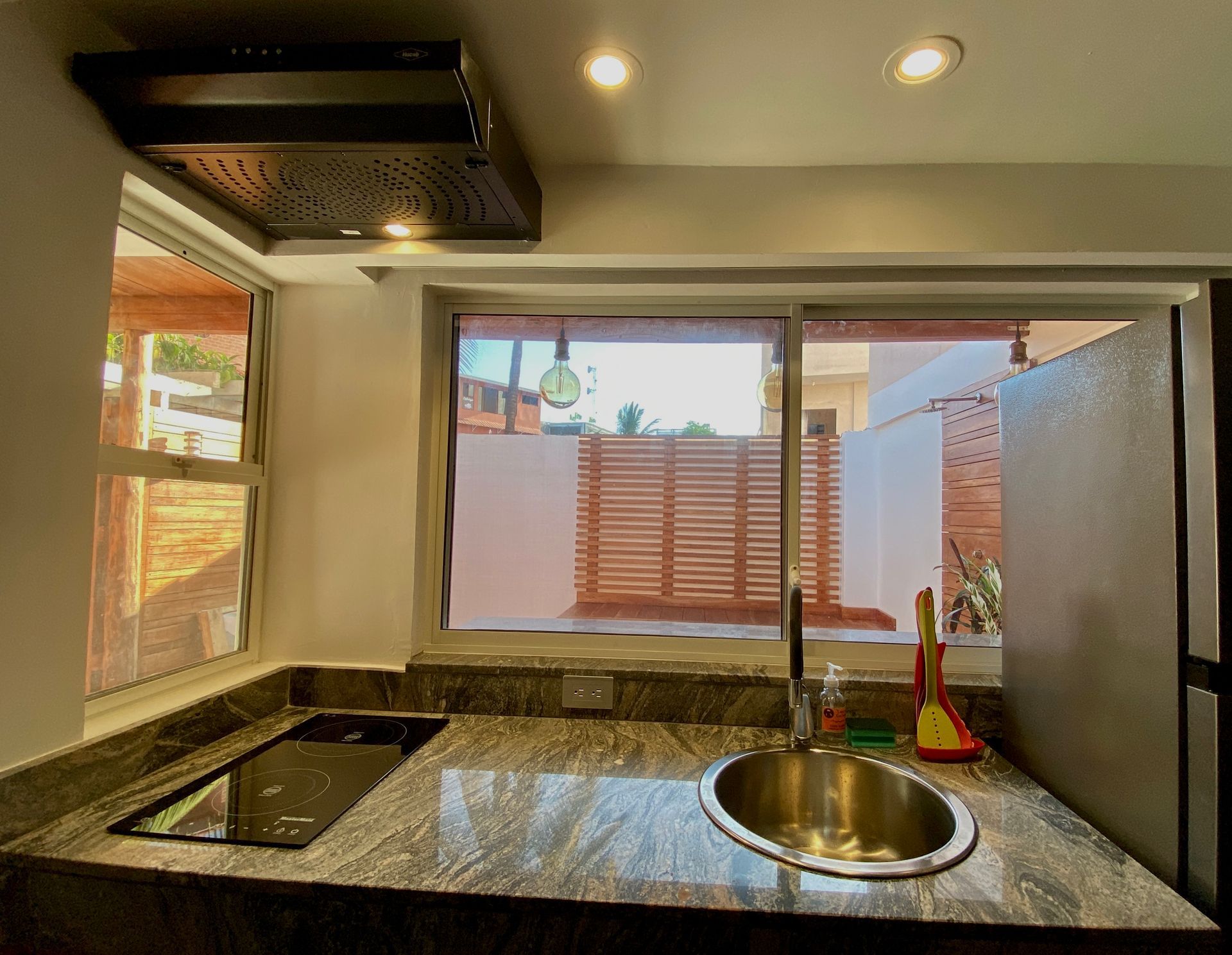 Galapagos hotel Kitchen with granite countertop, sink, and cooktop, looking out to a small yard through a sliding window.