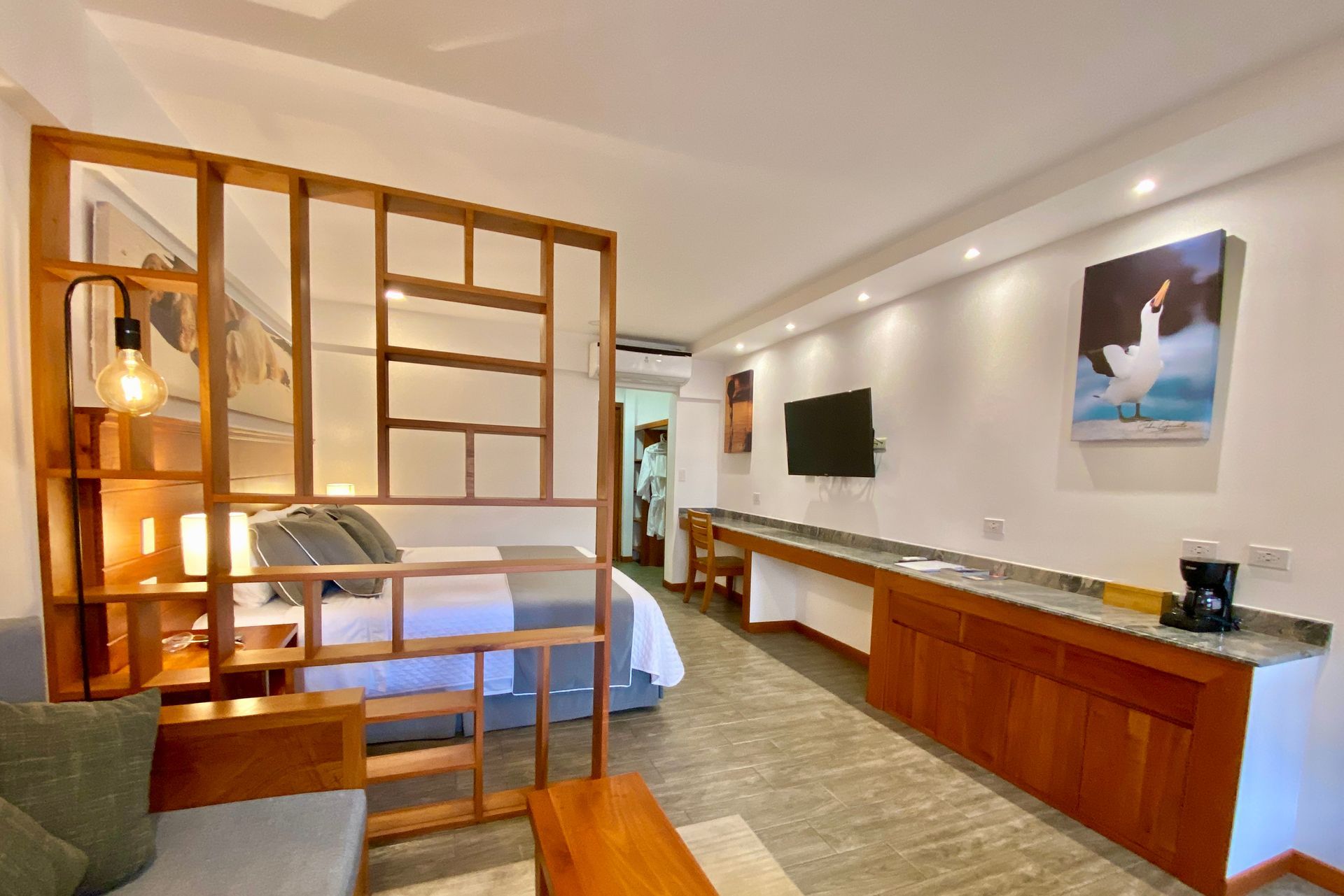 A Galapagos hotel studio apartment with a wooden divider separating the bed from the sitting area; a TV, desk, and artwork are visible.