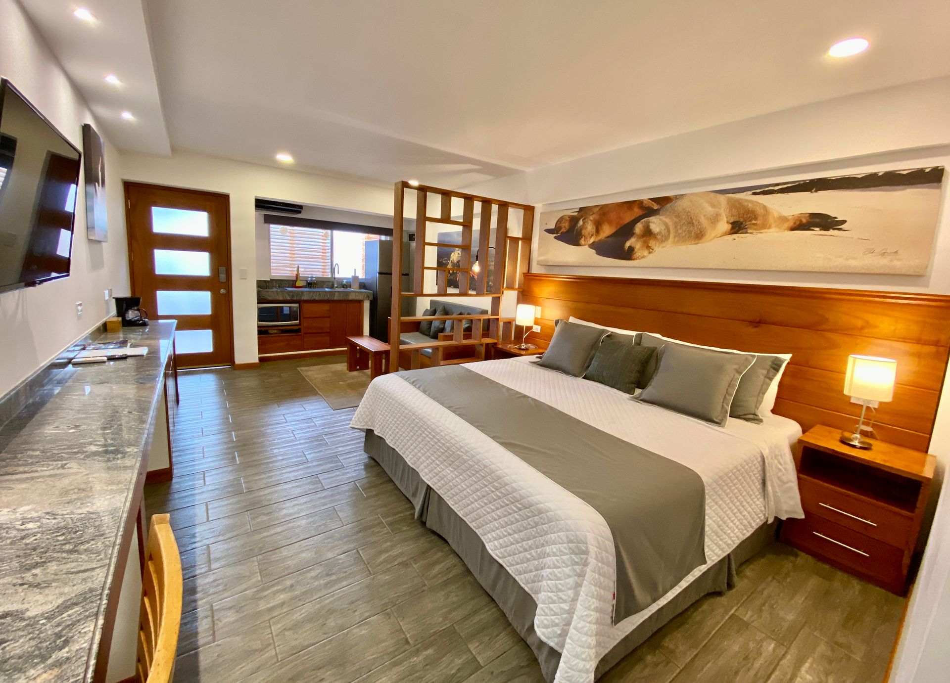 A Galapagos hotel suite with a large bed, a small kitchen, and a sitting area with a wooden divider. Neutral tones and natural light.