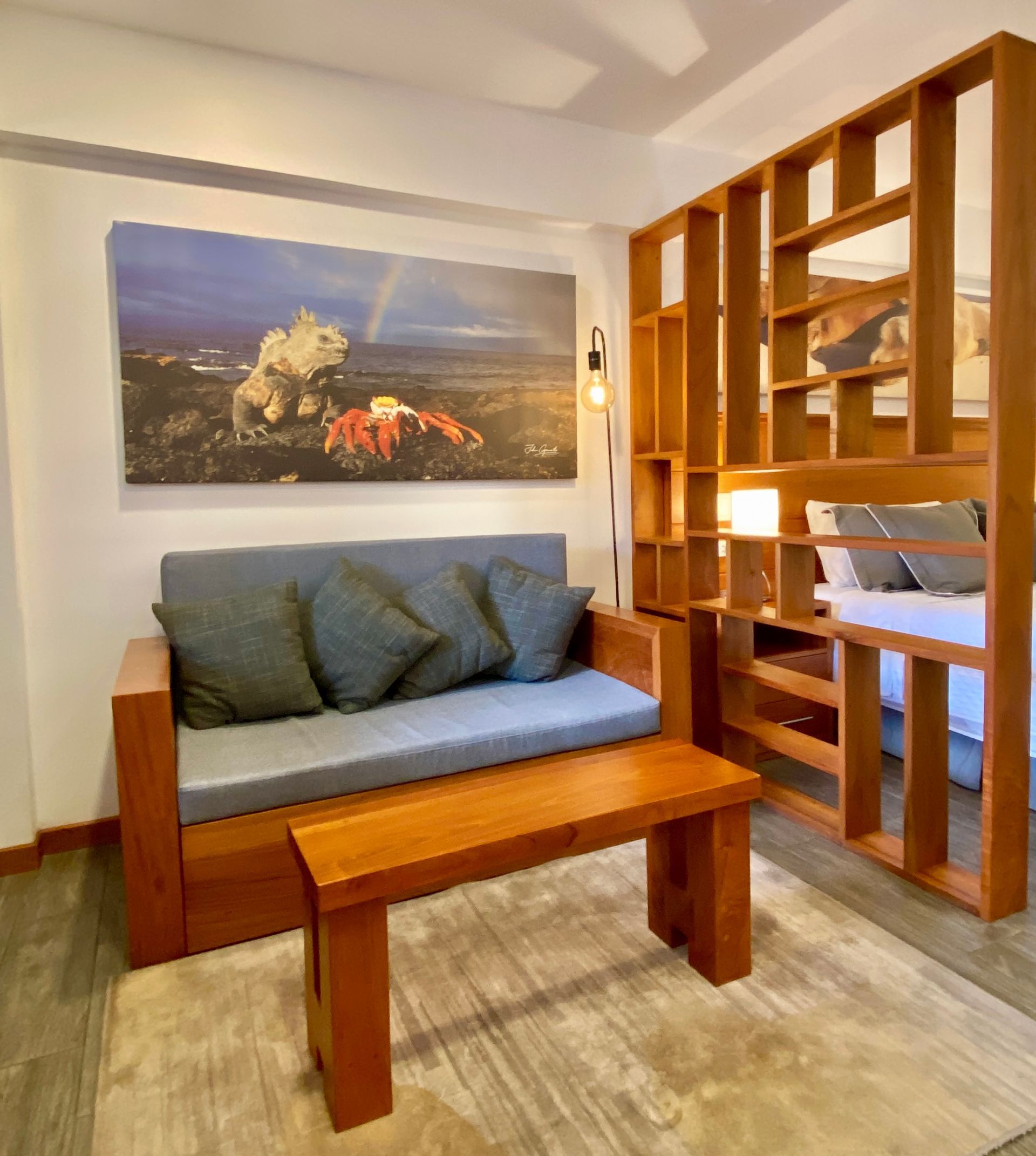A Galapagos hotel Living area with wooden couch, coffee table, and bookshelf-style room divider. Painting of a landscape with a rainbow.