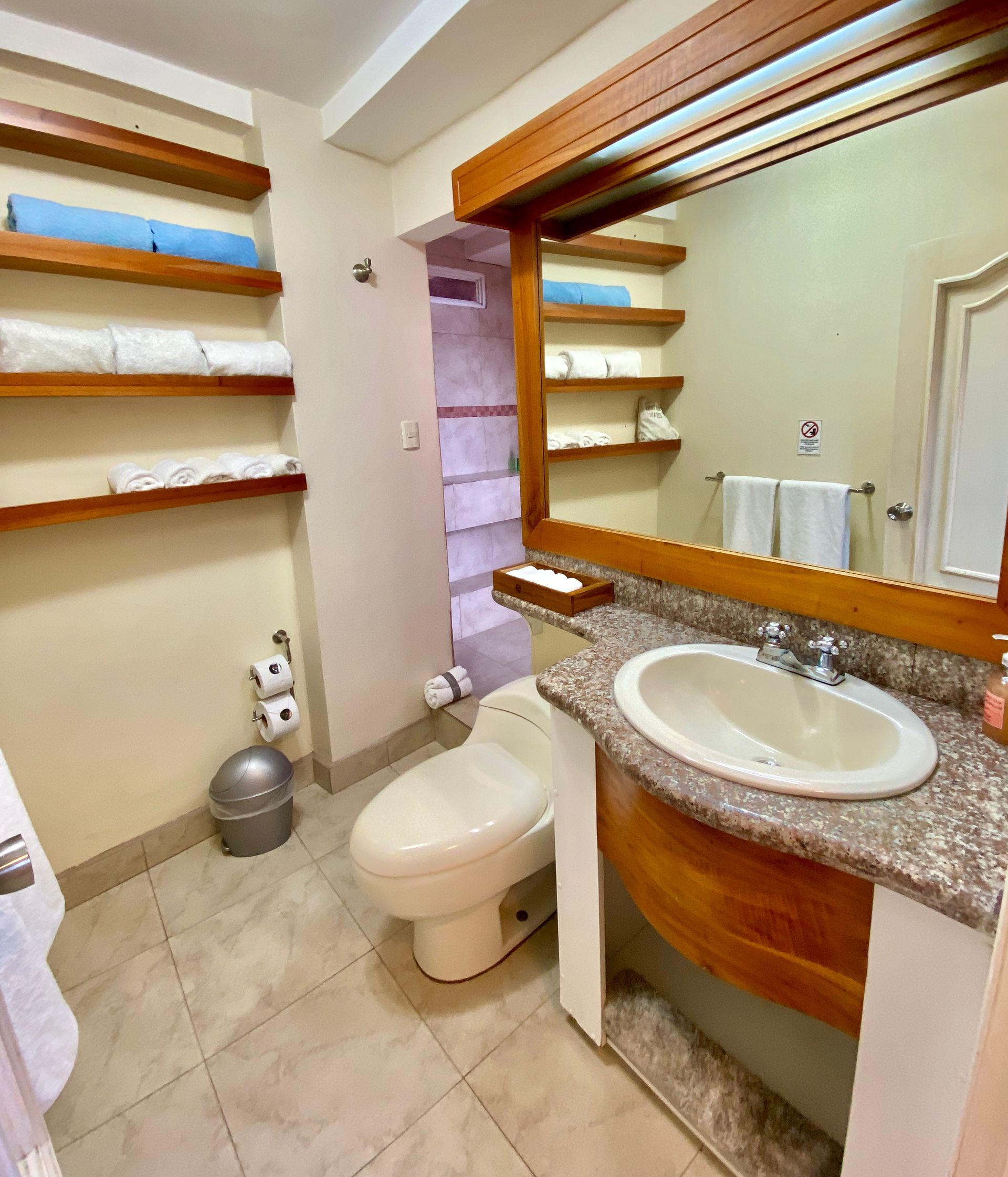 Galapagos Hotel bathroom with toilet, sink, shelves, and beige tile walls and floor.
