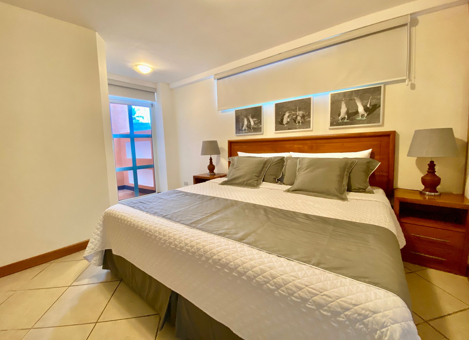 Bright hotel bedroom with a neatly made bed, wooden nightstands, lamps, and wall art near a window in the Galapagos Islands.