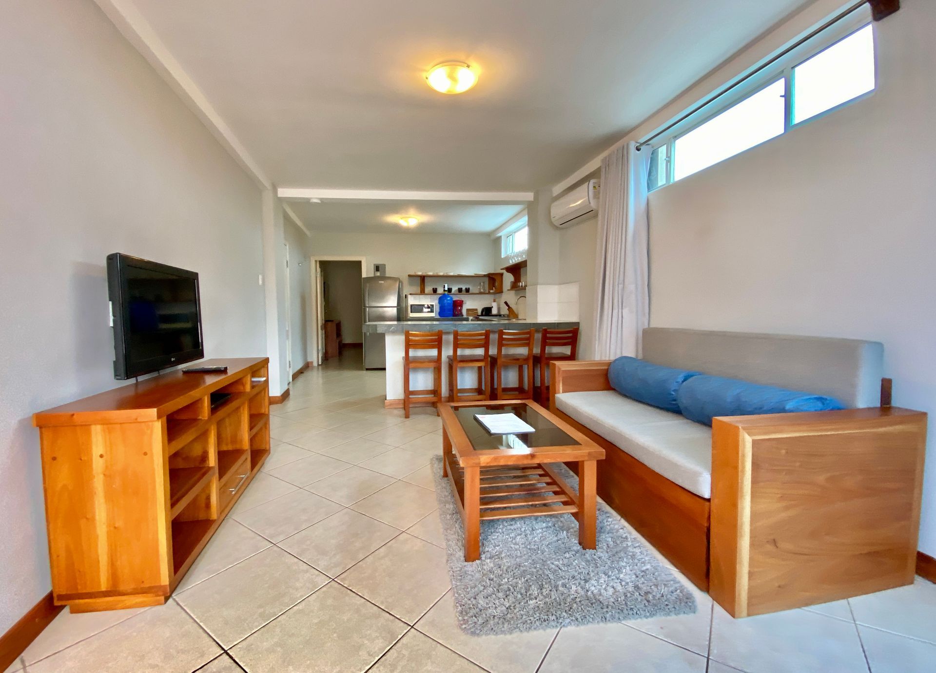 Bright hotel living room with blue sofa, wooden TV stand, coffee table, and open kitchen area in the Galapagos Islands