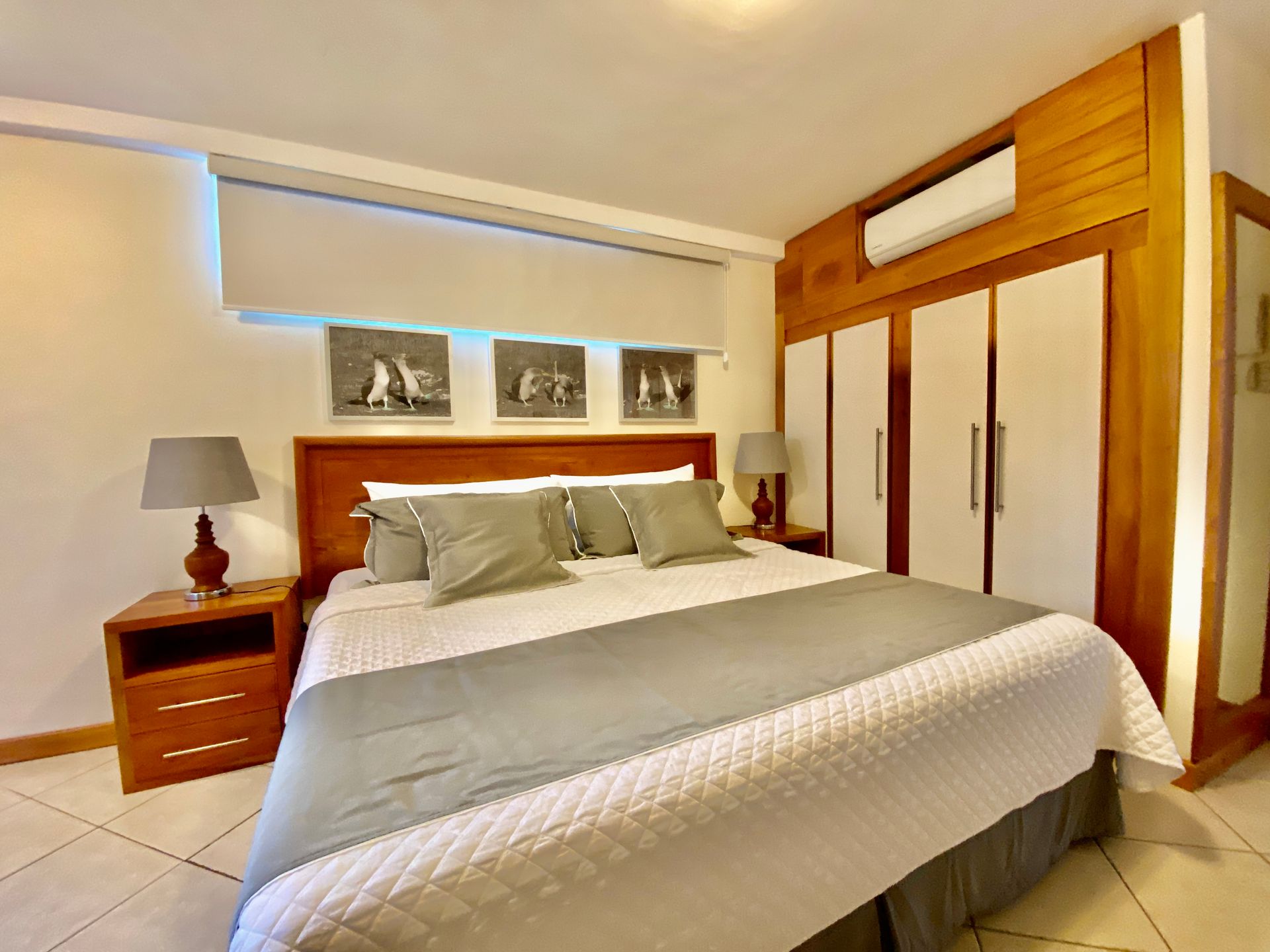 Bright Galapagos hotel bedroom with a large bed, wooden furniture, white wardrobe, and framed wall art