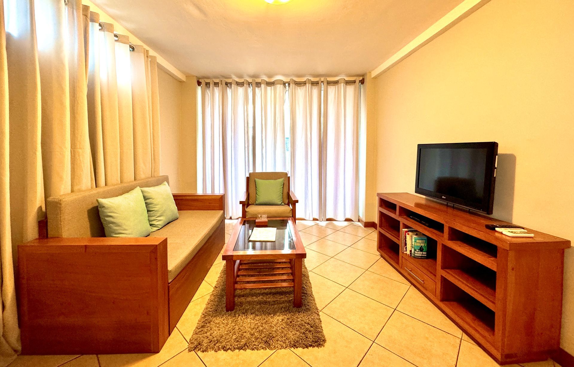 Bright Hotel living room with a wooden sofa, chair, coffee table, TV stand, and floor-to-ceiling curtains in the Galapagos Islands.