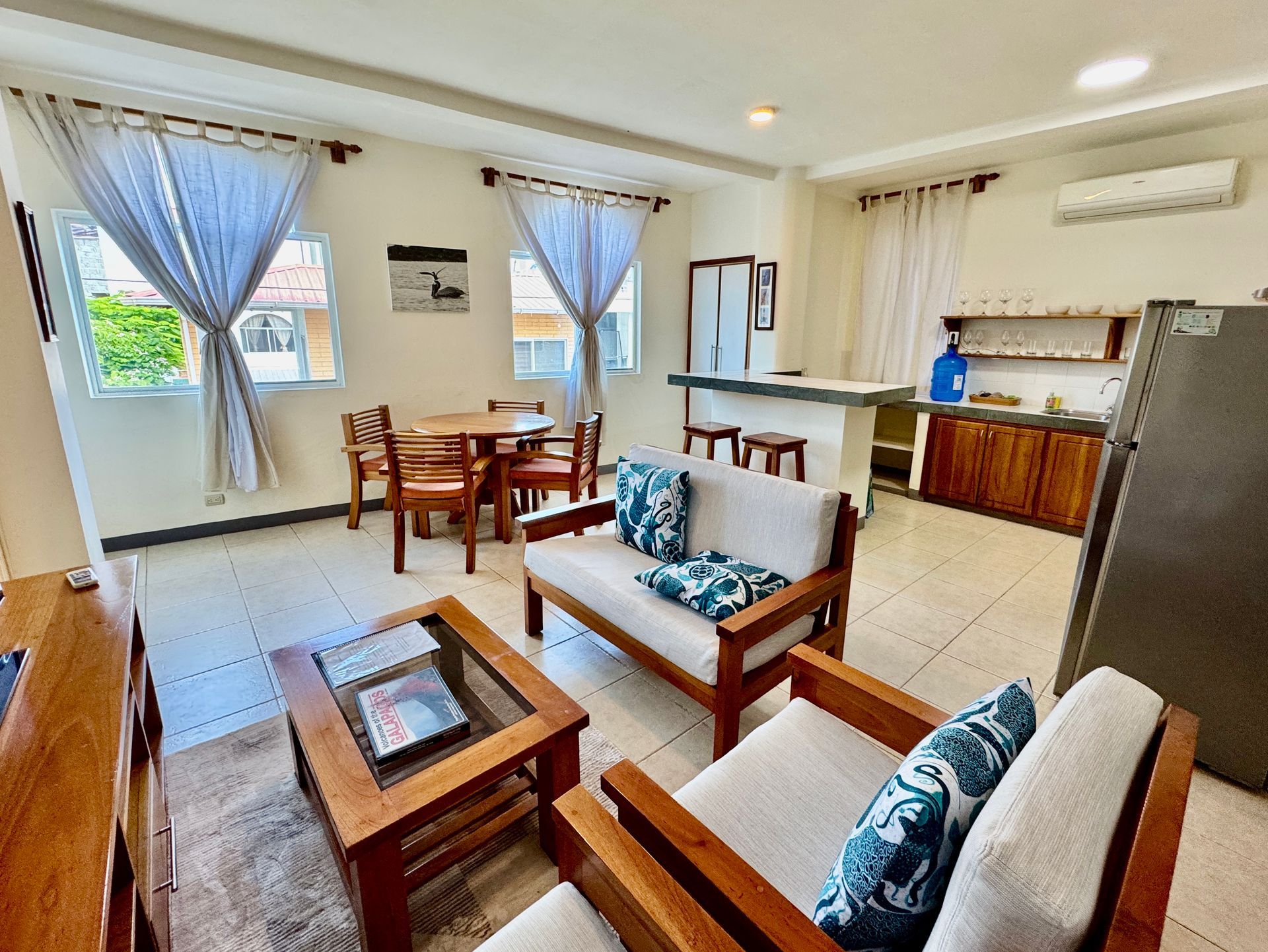 Bright Galapagos hotel living room with wooden furniture, blue curtains, kitchen counter, and air conditioner