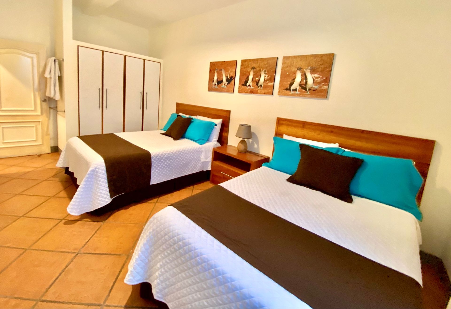 Two beds in a room with brown and white bedding, turquoise pillows, and artwork above the beds.