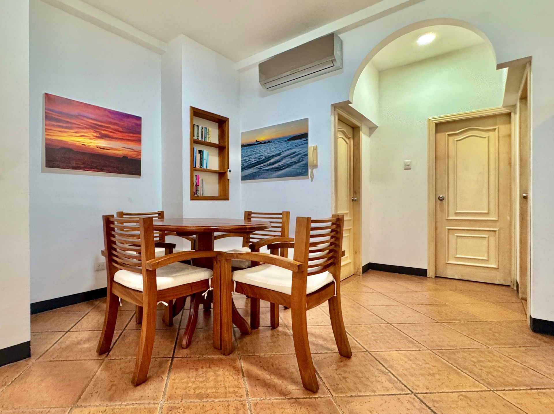 A Galapagos hotel dining area with a wooden table and chairs, artwork on the walls, and doorways leading to other rooms.
