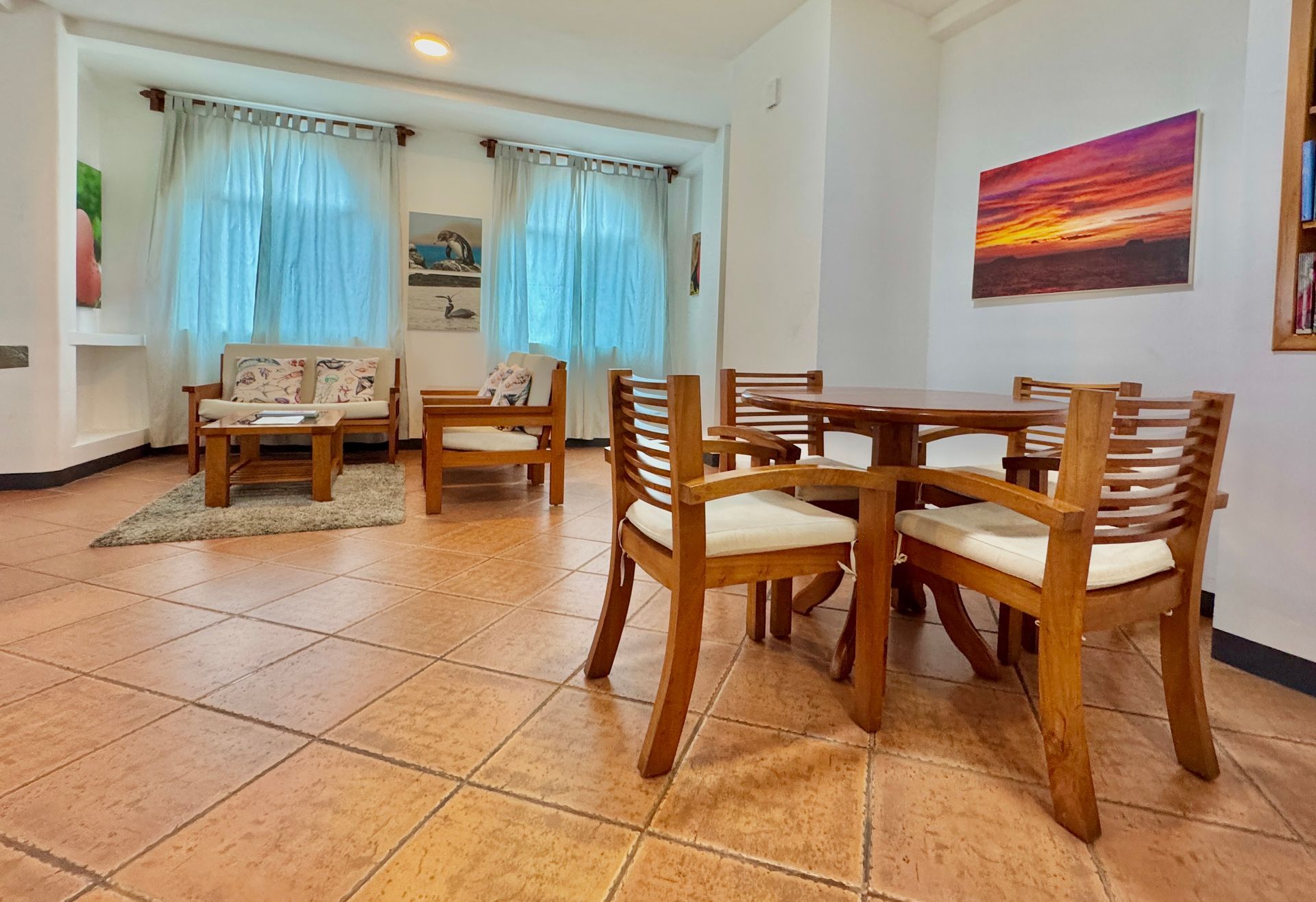 A well-lit Galapagos hotel living room with a dining set, sofa, and artworks. Natural light streams through sheer curtains.
