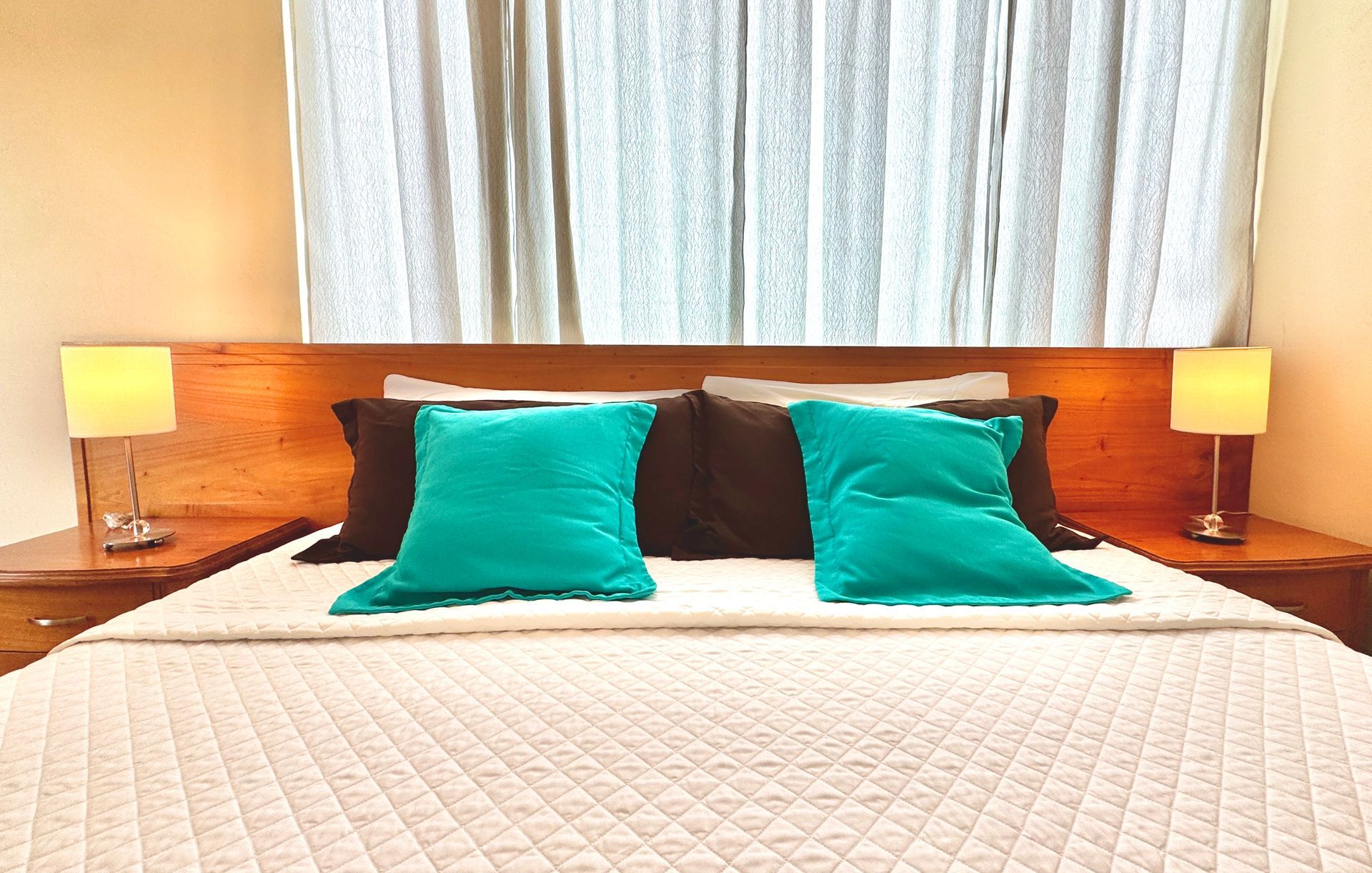 Galapagos hotel Bedroom with wooden headboard, two teal pillows, brown pillows, and two lamps on bedside tables.